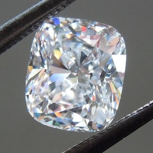 Puede incluir: Una piedra preciosa de diamante de talla coj&iacute;n, transparente, con una superficie brillante y multifac&eacute;tica.
