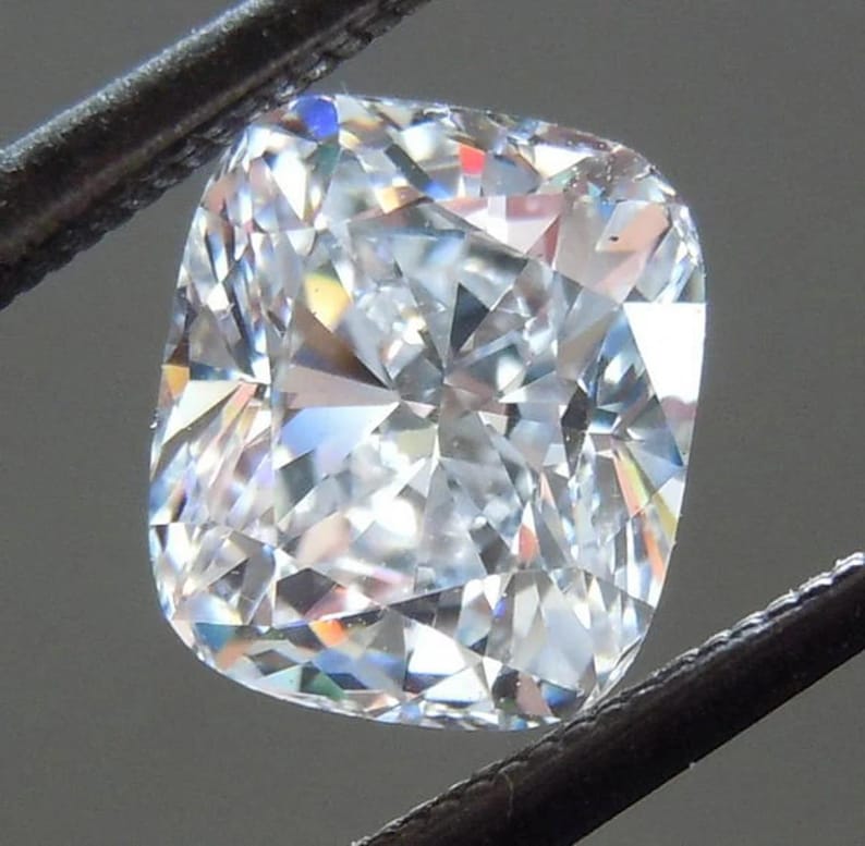 Puede incluir: Una piedra preciosa de diamante de talla coj&iacute;n, transparente, con una superficie brillante y multifac&eacute;tica.