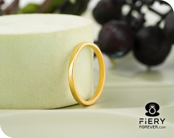 May include: A gold wedding band. The ring is a simple, thin band with a polished finish. The ring is set against a light green background with a blurred background of dark grapes.