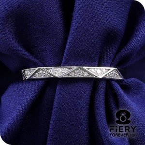 Puede incluir: Un anillo de banda de plata con un diseño geométrico que presenta una fila de pequeñas piedras de circonita cúbica transparentes.