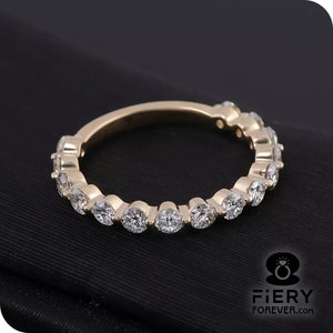 Puede incluir: Un anillo de banda de oro con una fila de diamantes redondos y transparentes engastados en pavé.