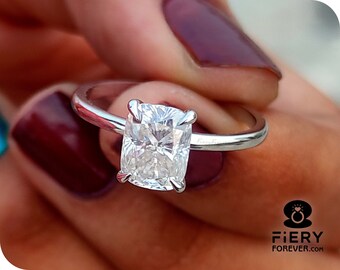 May include: A silver ring with a large, clear, cushion-cut diamond. The ring is set on a thin band.