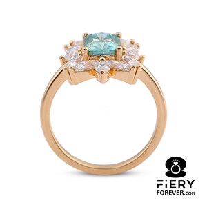 May include: A gold ring with a large, square, light blue gemstone surrounded by smaller, clear gemstones. The ring has a delicate, floral design.