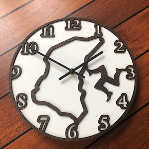 Puede incluir: Un reloj de pared redondo con esfera blanca y marco de madera marrón oscuro. El reloj presenta un diseño único con números recortados y una figura estilizada. Las manecillas del reloj son negras.