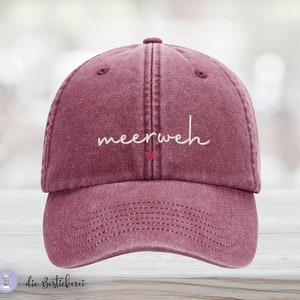 Könnte beinhalten: Eine marineblaue Baseballkappe mit dem Wort "meerweh" in weiß gestickt und einem kleinen roten Herz über dem Wort.