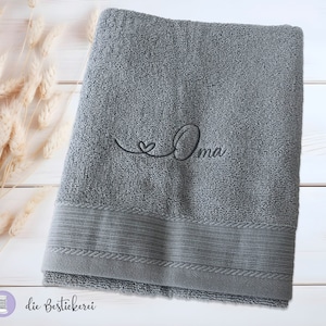May include: A gray bath towel with a black embroidered heart and the word "Oma" on it.