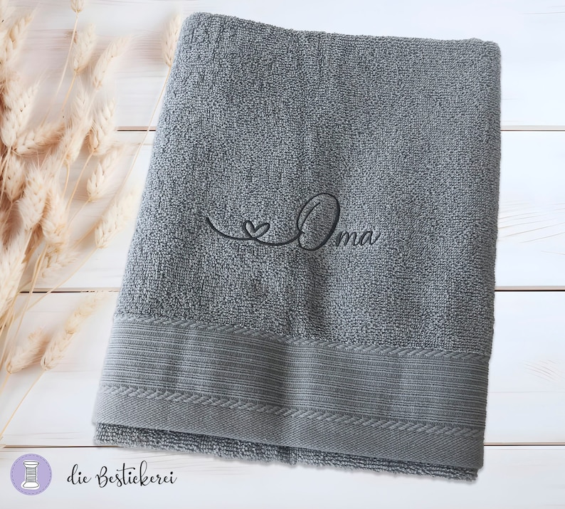 May include: A gray bath towel with a black embroidered heart and the word "Oma" on it.