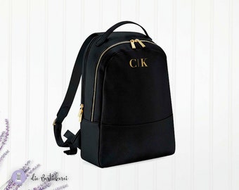 Könnte beinhalten: Schwarzer Rucksack mit goldenen Reißverschlüssen und einem goldenen Monogramm mit der Aufschrift "C|K".