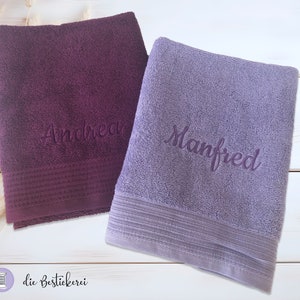 May include: Two personalized towels, one purple with the name "Andrea" embroidered on it and one light purple with the name "Manfred" embroidered on it.