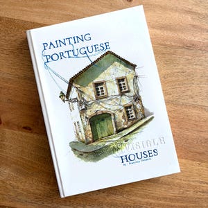 Może przedstawiać: Książka zatytułowana "Painting Portuguese Invisible Houses" autorstwa Francisco Fonseca. Okładka przedstawia akwarelową ilustrację budynku z zielonymi drzwiami i oknami. Tytuł jest niebieski na białym tle.