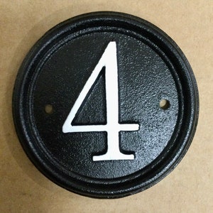 May include: Black circular house number plaque with a white number "4" in the centre. The plaque has a raised rim.