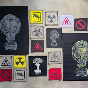 Könnte beinhalten: Sammlung schwarzer Stoffaufnäher mit verschiedenen Designs. Enthält eine Gasmaske, einen Pilz, Gefahrensymbole und ein außerirdisches Raumschiff. Die Aufnäher sind in Schwarz, Weiß, Gelb, Rot und Grau gehalten.