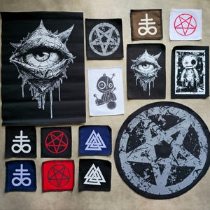 May include: Collection of patches with various occult and gothic designs. Includes a large black banner with an eye graphic, patches with pentagrams, sigils, and a voodoo doll. The color palette is primarily black, white, and gray.