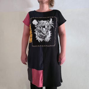 Peut inclure: Robe noire, longueur genou, avec un graphique de rat menaçant. La robe présente des panneaux colorés noirs, roses et jaunes. Le graphique du rat est encadré d'une bordure cousue.