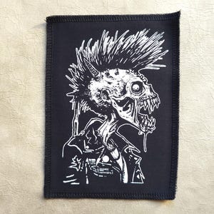 Pode incluir: Patch preto e branco com uma ilustração de zumbi punk rock. O zumbi tem um mohawk e está vestindo uma jaqueta de couro.