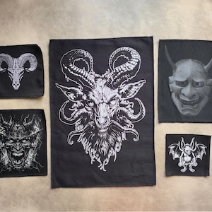 May include: A selection of black patches with white illustrations. The patches depict a goat skull, a horned demon face, a Japanese demon mask, a bat-like creature, and a goat-like demon with large horns and a beard.