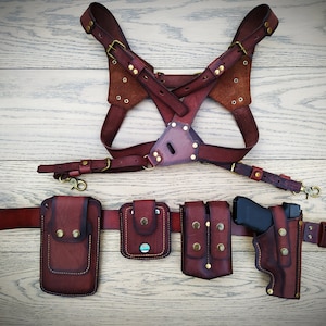 Pode incluir: Um conjunto de coldres de couro castanho com um arnês de peito, cinto e várias bolsas. O conjunto inclui um coldre para uma pistola, uma bolsa para carregador e duas bolsas adicionais.