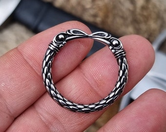 May include: A silver ring with a braided design and two bird-like heads at the top.
