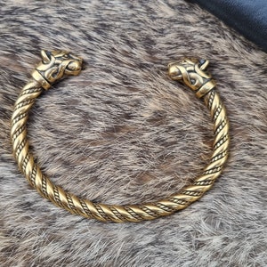 May include: A gold-toned metal bracelet with two wolf head ends. The bracelet is braided and has a detailed design.