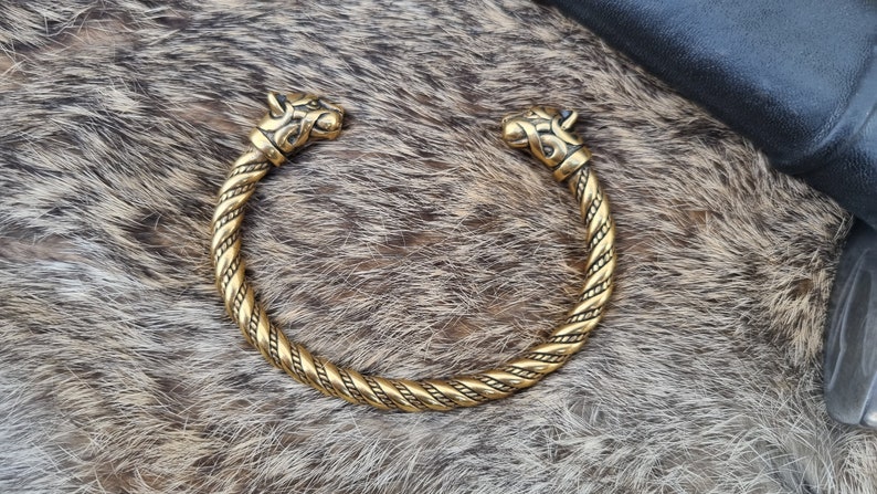 May include: A gold-toned metal bracelet with two wolf head ends. The bracelet is braided and has a detailed design.
