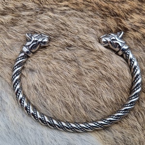 May include: A silver bracelet with two wolf heads at the ends. The bracelet is twisted and has a detailed design.