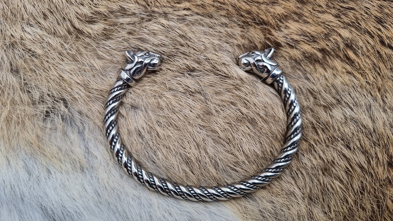 May include: A silver bracelet with two wolf heads at the ends. The bracelet is twisted and has a detailed design.