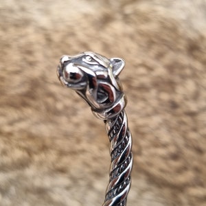 May include: A silver bracelet featuring a detailed wolf head design. The bracelet is twisted and has a polished finish.