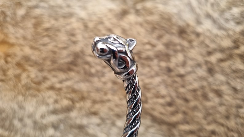 May include: A silver bracelet featuring a detailed wolf head design. The bracelet is twisted and has a polished finish.