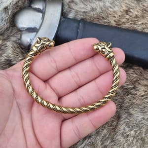 May include: A gold-toned Viking-style bracelet with twisted rope design and wolf head terminals.
