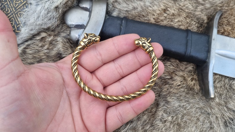 May include: A gold-toned Viking-style bracelet with twisted rope design and wolf head terminals.