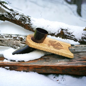 Peut inclure: Un support en bois avec un motif sculpté d'un oiseau et une coupe à boire en corne noire. Le support repose sur une bûche recouverte de neige.