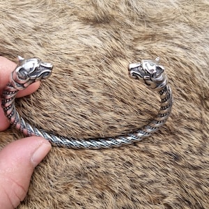 May include: A silver bracelet with two wolf head ends. The bracelet is twisted and has a braided design.