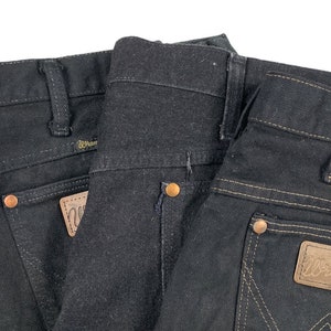 May include: Two pairs of black denim jeans with a brown leather patch on the back pocket that says "Wrangler".