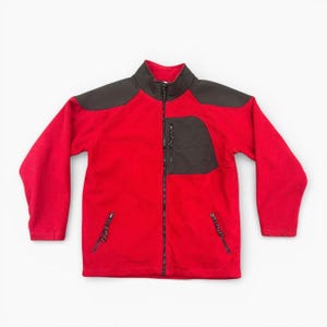 Peut inclure: Veste polaire rouge avec col, empiècements épaules et poche poitrine noirs. La veste a une fermeture éclair intégrale et deux poches latérales zippées. Conçue pour les activités de plein air.