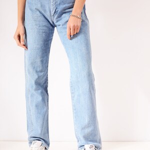 Op de afbeelding: Lichtblauwe denim jeans met een rechte pijp. De jeans heeft een hoge taille en een knoopsluiting. Het model draagt witte sneakers.