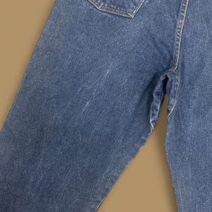 K&ouml;nnte beinhalten: Nahaufnahme einer blauen Jeans. Die Jeans weist Gebrauchsspuren auf, mit sichtbaren Ausbleichungen und hellen Flecken. Die N&auml;hte sind entlang der N&auml;hte und Taschen sichtbar. Der Gesamteindruck ist l&auml;ssig und vintage.