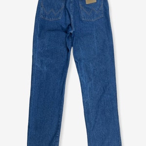 K&ouml;nnte beinhalten: Eine blaue Jeans aus Denim mit einem braunen Leder-Patch auf der Ges&auml;&szlig;tasche, auf dem "Wrangler" steht.