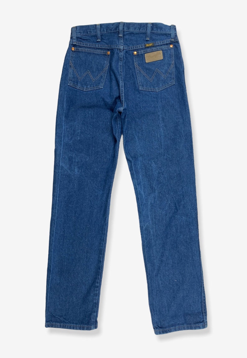K&ouml;nnte beinhalten: Eine blaue Jeans aus Denim mit einem braunen Leder-Patch auf der Ges&auml;&szlig;tasche, auf dem "Wrangler" steht.