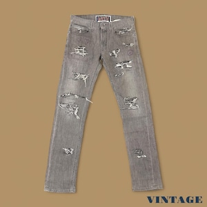 Può includere: Jeans di denim grigio con dettagli strappati, con strappi e toppe multiple. I jeans hanno un classico design a cinque tasche e un'etichetta Levi's. Piccoli scarabocchi sono visibili sui jeans. La parola "VINTAGE" è in basso.