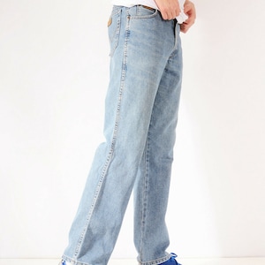 May include: A person wearing light blue denim jeans with a white t-shirt and blue trainers with a zebra print.