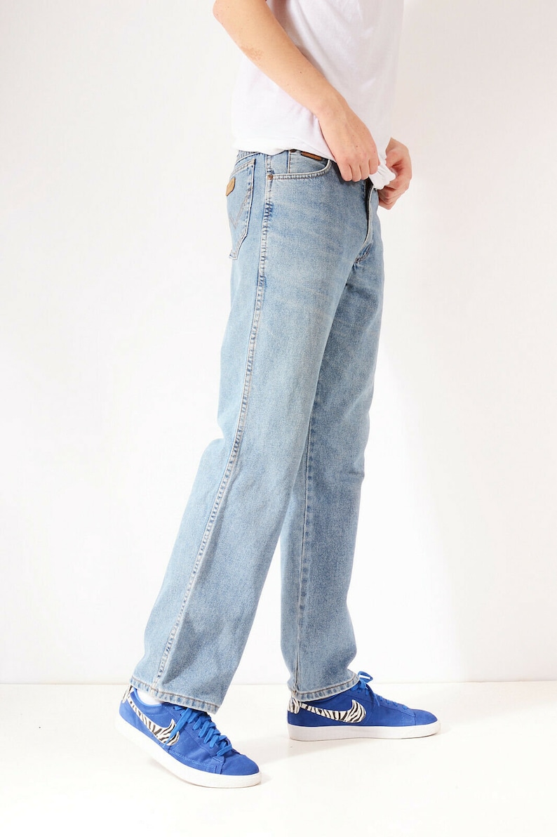 May include: A person wearing light blue denim jeans with a white t-shirt and blue trainers with a zebra print.