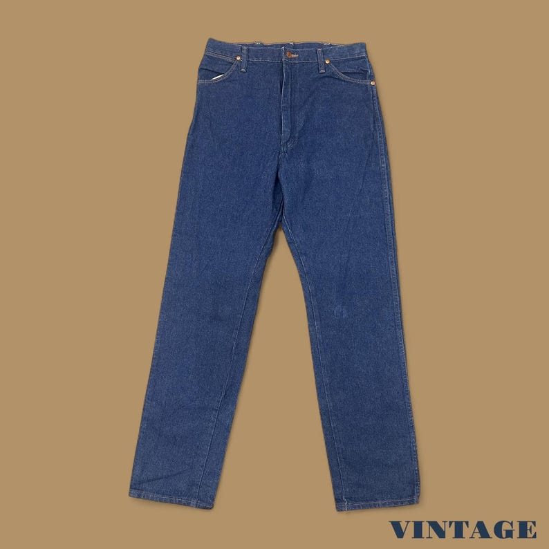 May include: Blue denim jeans with a classic five-pocket design. The jeans have a straight leg cut and a button and zipper closure. The word "VINTAGE" is printed in white at the bottom right corner.