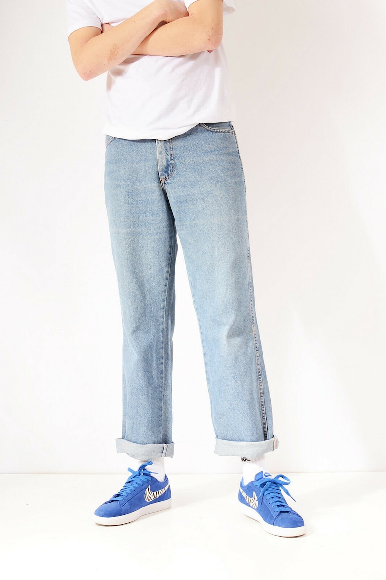 May include: A person wearing light blue denim jeans with a white t-shirt and blue trainers with a zebra print swoosh.