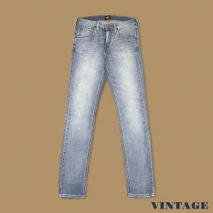 May include: Light blue denim jeans with a classic five-pocket design. The jeans have a faded wash and a straight leg fit. The Lee logo is visible on the back pocket. The word "VINTAGE" is at the bottom right.