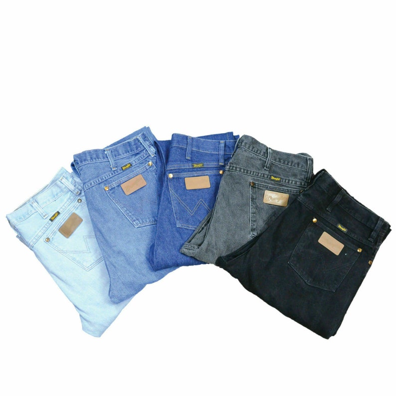 May include: Five pairs of blue jeans in different shades of blue, gray, and black. Each pair has a brown leather patch with the word "Wrangler" on it.