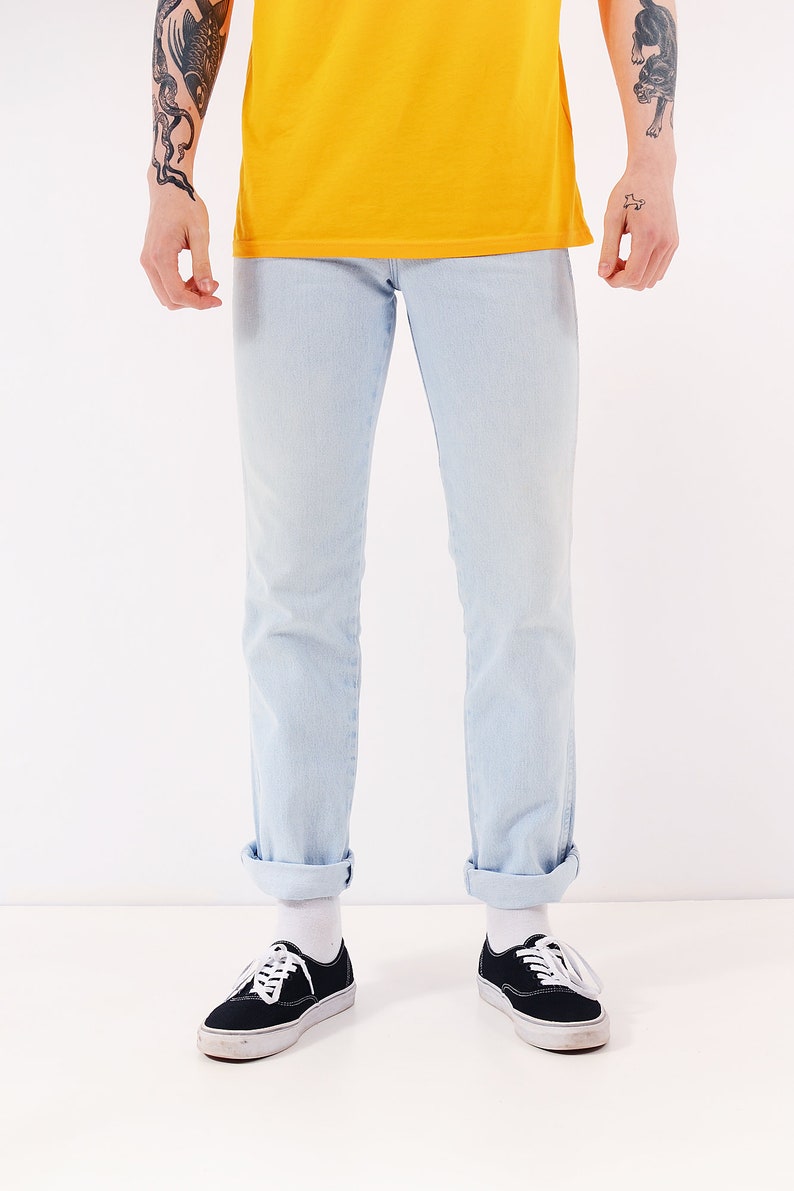 May include: A person wearing light blue jeans with the cuffs rolled up and black canvas sneakers with white laces.