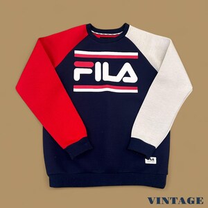 May include: A navy blue FILA sweatshirt with red sleeves and a gray sleeve. The FILA logo is in white with red stripes. The word "VINTAGE" is at the bottom.