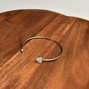 Peut inclure: Un bracelet jonc argenté avec un charme en forme de cœur incrusté de strass transparents.