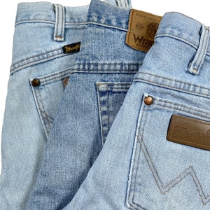 Puede incluir: Tres pares de pantalones vaqueros de mezclilla azul con diferentes bolsillos traseros y etiquetas. Los vaqueros tienen un lavado claro y est&aacute;n doblados uno encima del otro.