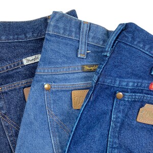 Op de afbeelding: Twee paar blauwe denim jeans met het Wrangler-logo op de achterzakken. De jeans zijn gevouwen en op elkaar gestapeld.